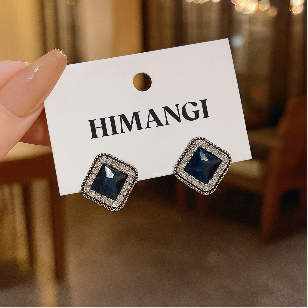 Sapphire Square Stud Earrings on a 'HIMANGI' branded card held by a hand.