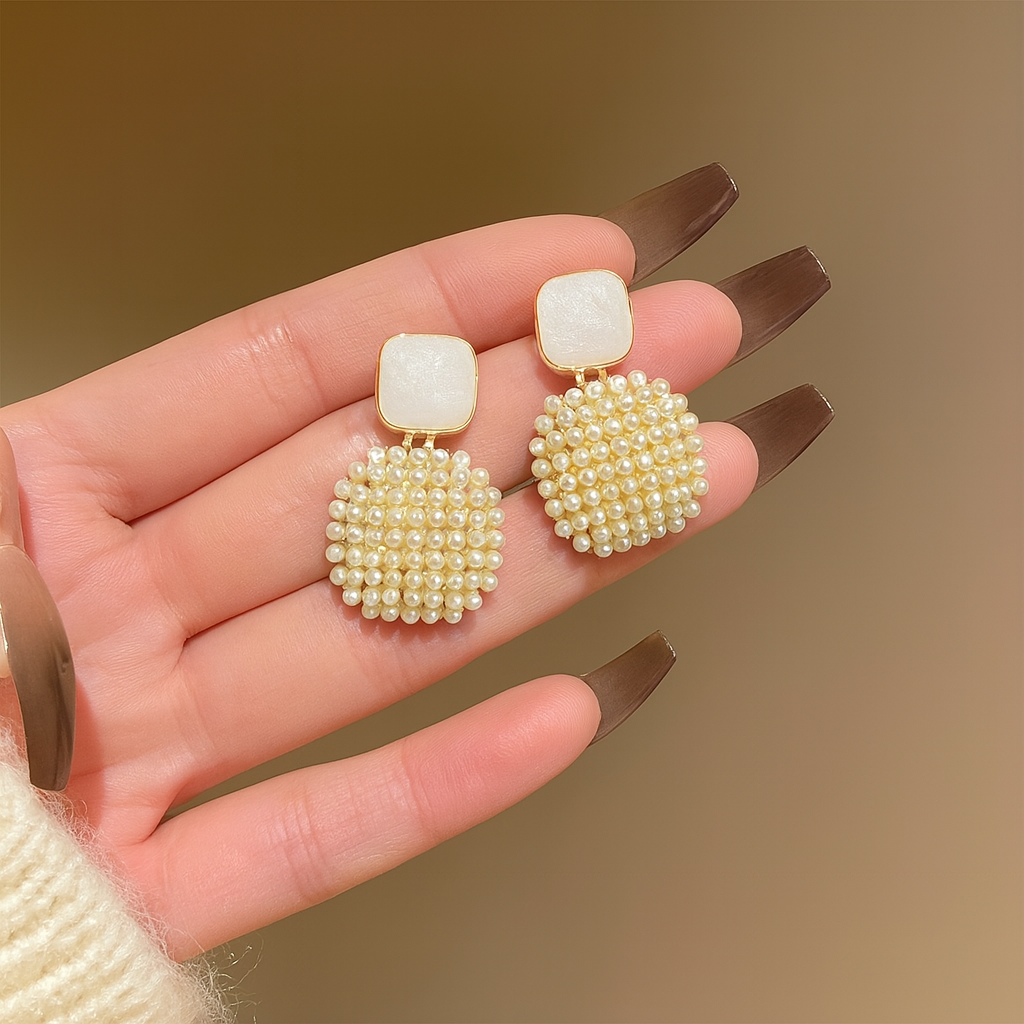 Ivory Pearl Cluster Drop Earrings held in a hand with a brown background