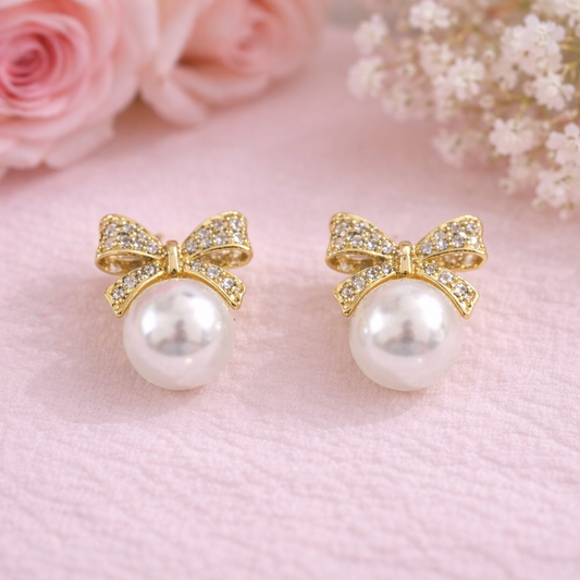 Pearl earrings with gold bows on a pink background with flowers